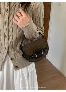 Bolso silla de gamuza marrón con correas de cuero negro sobre un suéter de punto