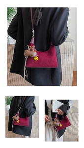 Detail of burgundy crescent shoulder bag in matte suede with dual charms and leather strap