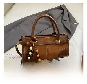 Detail of brown leather and suede crossbody bag with beaded charm and top handle