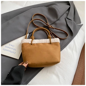Nahaufnahme der braunen Wildleder-Beuteltasche mit weißem Pelzbesatz auf grauem Blazer