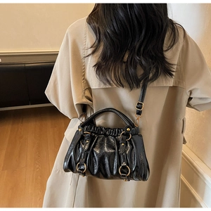 Detail of black ruched crossbody bag with glossy texture and elegant gold ring hardware