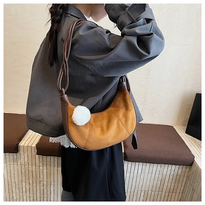 Détail du sac hobo en daim marron avec garniture en cuir et pompon blanc décoratif