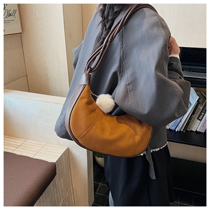 Detail of caramel suede crescent hobo bag with white pompom charm in home setting