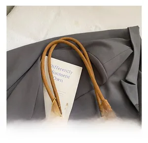 Gros plan du sac fourre-tout en daim marron avec pompon rouge et pendentif à carreaux