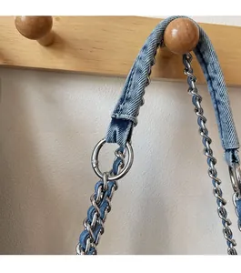 Detail of woven denim fabric and silver metal chain strap on a wooden hook