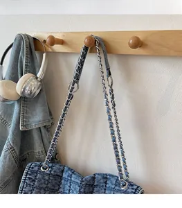 Detail of light blue quilted denim shoulder bag with woven metal chain on wooden rack