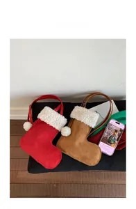 Detailed view of red and brown suede Christmas stocking shaped crossbody bags on soft mat