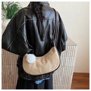 Détail du sac demi-lune en daim kaki avec bordure en cuir marron et pompon blanc