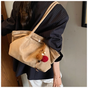 Détail d'un grand sac cabas en daim marron avec plis et breloques en boules de poils