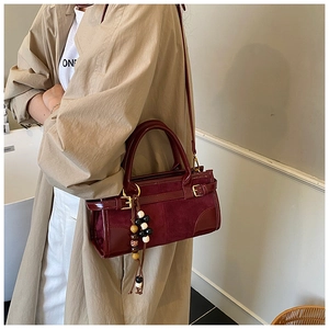 Borsa baguette bordeaux con ciondolo di perline, indossata da una modella in trench