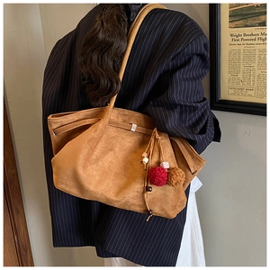 Detailed close-up of brown suede tote bag with plush pompom and wooden bead charm