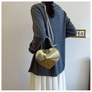 Modella che indossa una borsa a tracolla a forma di cuore dorata sopra un maglione grigio