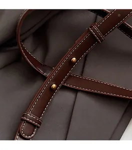 Close-up of brown leather strap with contrast white stitching and gold metal rivets