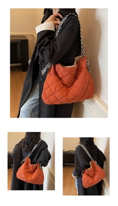 Close-up of orange quilted tote bag featuring a black and white striped scarf strap