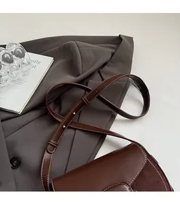 Close-up of adjustable brown leather shoulder strap with golden metal buckle and white stitching
