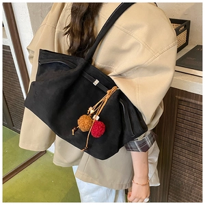 Détail du sac cabas en daim noir avec un pompon coloré et une boucle métallique chic
