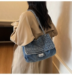 Detailed view of blue denim shoulder bag featuring quilted texture and silver chain strap