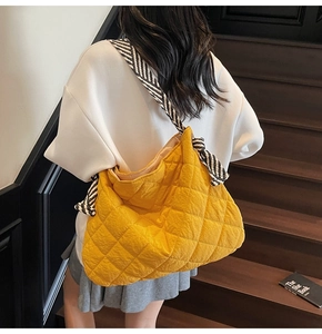 Detail of yellow quilted tote bag with black and white striped woven strap and knot design