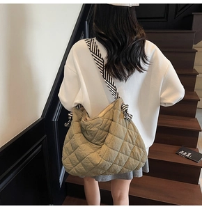 Detail of quilted olive tote bag featuring a striped wide shoulder strap and puffy texture