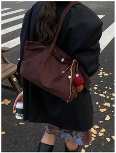 Détail du cabas en daim marron foncé avec un gland décoratif à perles et un pompon rouge
