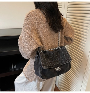 Detailed view of black denim quilted chain bag worn over a brown knit sweater