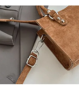 Detail of premium caramel suede texture and polished silver metal hardware on a women's handbag