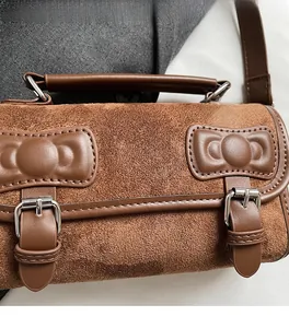 Close-up of brown suede pillow bag with dual bow detailing and metal buckle closure