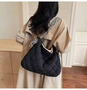 Quilted tote bag with black and white striped shoulder strap worn on a trench coat