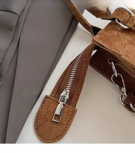 Detail of smooth silver zipper and metallic hook on brown suede crossbody bag