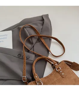 Detail of adjustable shoulder strap and curved handle on brown suede crossbody bag