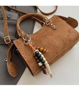 Macro detail of brown suede handbag with metal rivets and wooden bead tassel accessory
