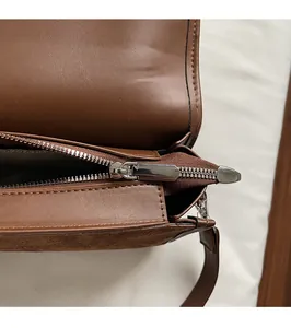 Detailed macro view of smooth silver metal zipper and brown leather texture on handbag
