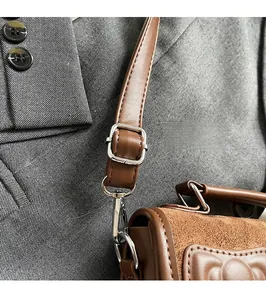 Detail of adjustable shoulder strap and metal hardware on brown suede crossbody bag