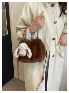Detail der dunkelbraunen Kunstpelz-Handtasche mit Plüschhasen-Anhänger am Trenchcoat