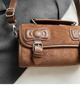 Detail of a brown Boston bag featuring frosted texture with 3D leather bows and silver buckles