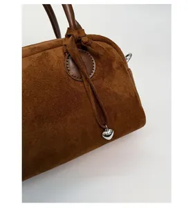 Primer plano de bolso de ante marrón con colgante de corazón plateado y detalle de cuero