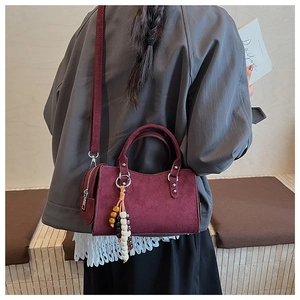 Détail du sac en daim bordeaux avec pompons en perles de bois et bandoulière réglable