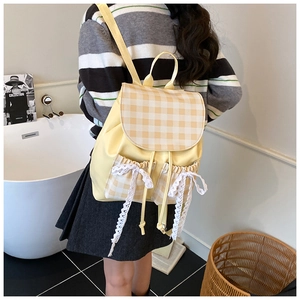 Detail of yellow plaid backpack featuring lace bows and drawstring closure in lifestyle setting