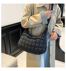 Detail view of a black quilted cloud crossbody bag worn with a beige trench coat