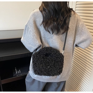 Detail of black faux shearling crossbody bag with leather strap on a model wearing grey sweater