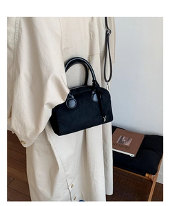 Close-up of black suede boston bag with round metal hardware on beige trench coat