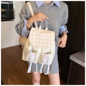 Detail of beige plaid backpack featuring lace bow accents worn by a model