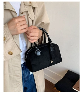 Detalle de un bolso Boston de ante negro con colgante de corazón plateado y asas redondas