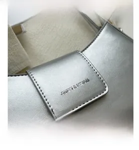 Close-up of metallic silver PU leather texture with brand embossing on the handbag