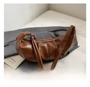 Detail of brown pleated moon bag with shiny leather texture and decorative knot strap