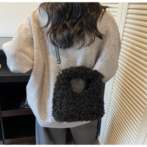 Close-up of black faux shearling crossbody bag with leather strap on a model