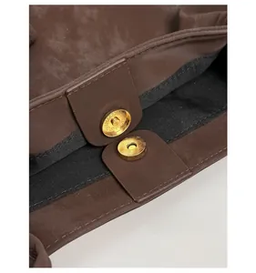 Detail view of the secure golden magnetic snap closure on a dark brown suede tote bag