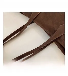 Close-up of the stitching and handle attachment on a brown matte suede tote bag