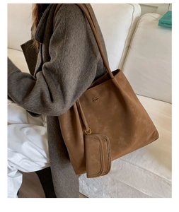 Close-up of brown textured tote bag with detachable pouch on a model in a warm setting