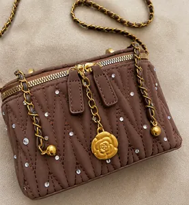 Détail du sac boîte matelassé marron avec pendentif camélia doré et bandoulière chaîne